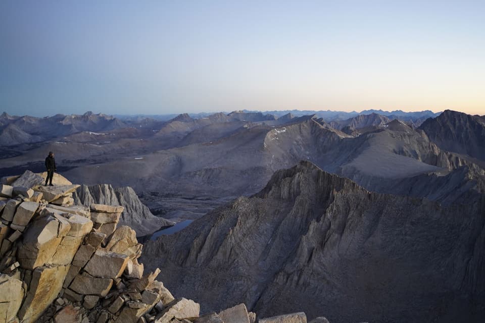 A lone hiker on a granite point above a sea of Sierra peaks, Whitney summit