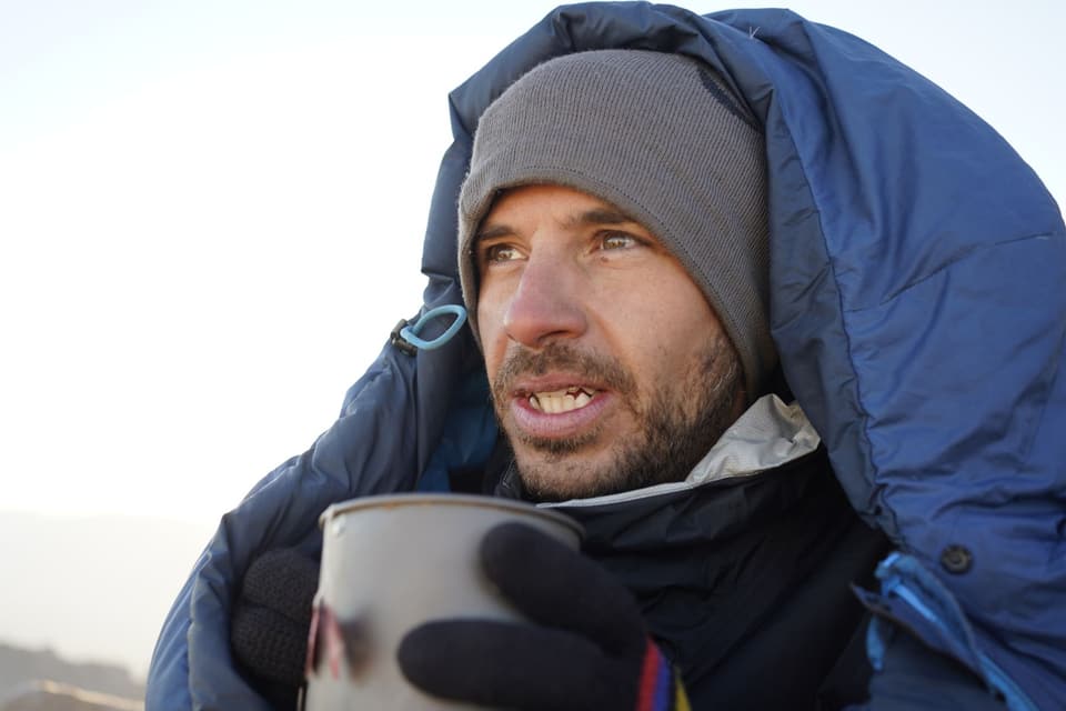 Wrapped in a sleeping bag on the summit holding a pot of hot food