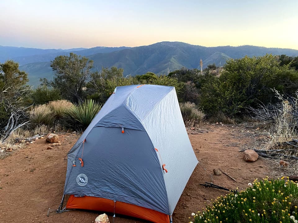 a grey and orange one-person tent on a desert ridge at sunset