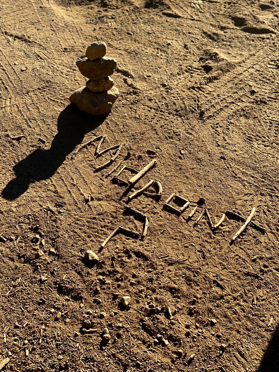 the word Midpoint spelled in sticks beside a small rock cairn on a dirt clearing