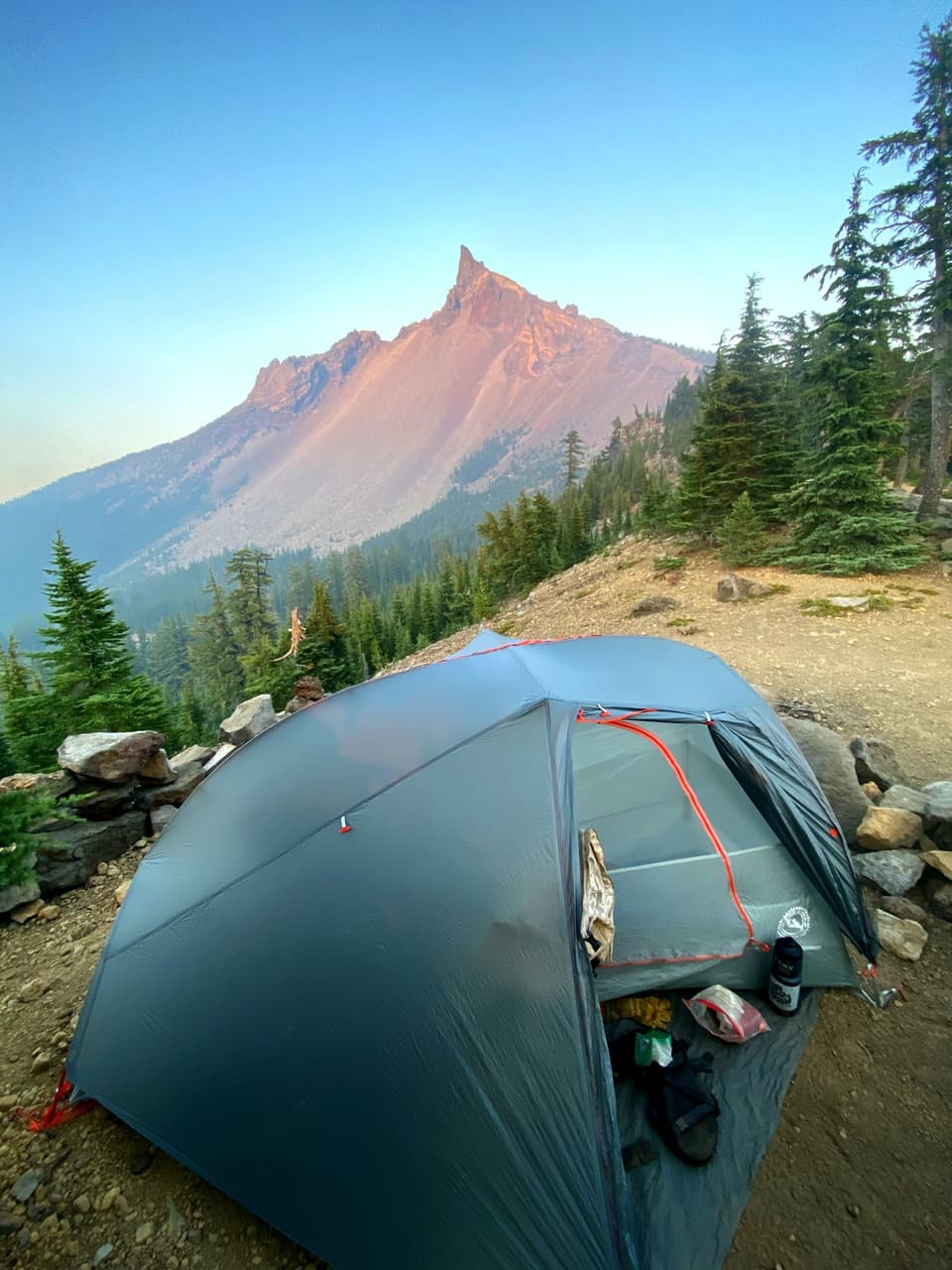 a grey one-person tent below a pointed peak glowing pink at sunset