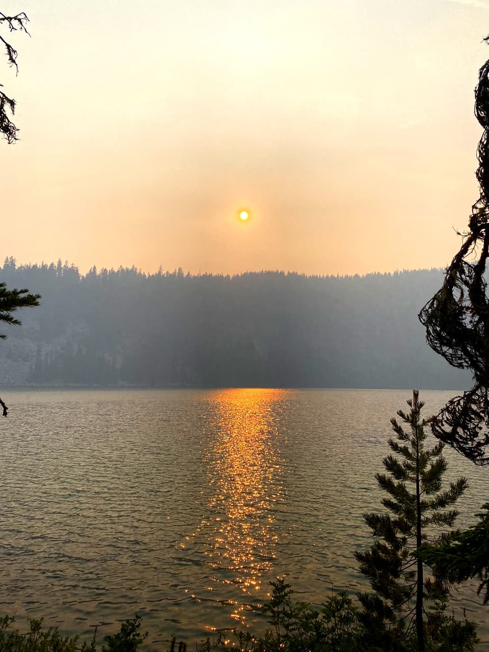 Smoke-red sun reflected in a mountain lake
