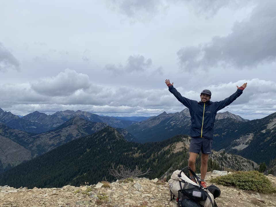 Atlas with his arms up on a rocky summit above the last North Cascades ridges, day 129