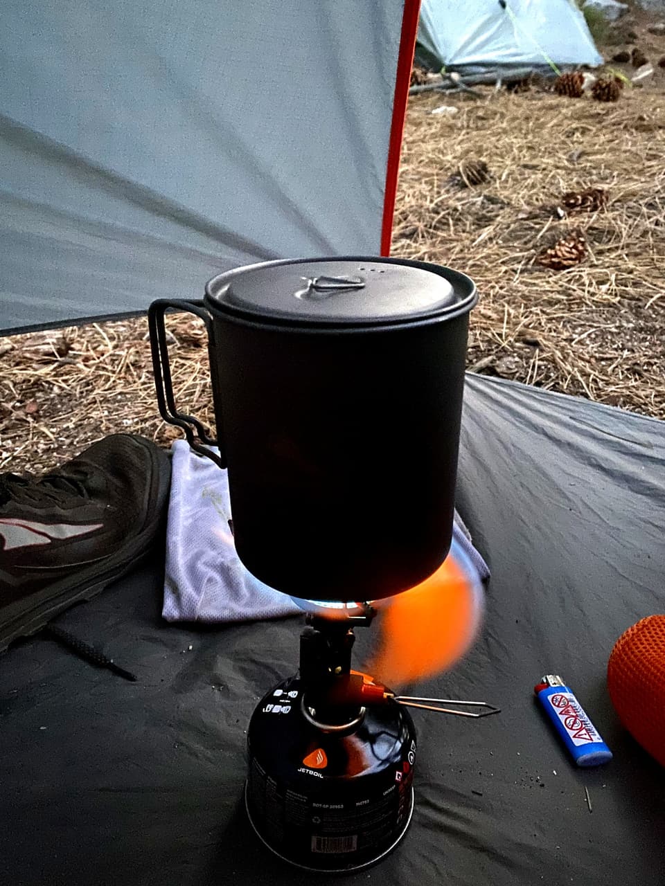 a titanium pot on a canister stove inside a tent vestibule at dawn