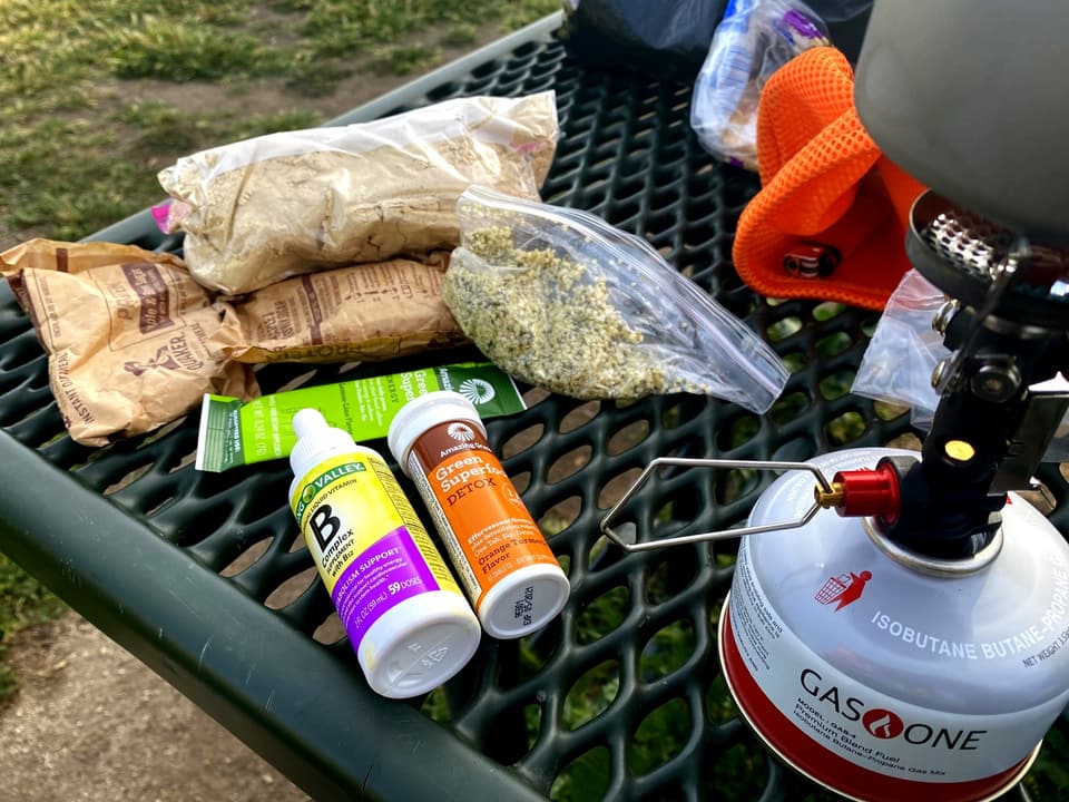 canister stove on a picnic table beside oatmeal packets and repacked food bags