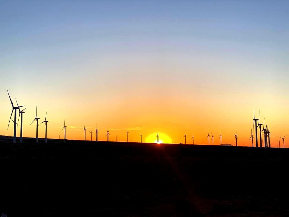 sunrise through a row of wind turbines above the trail